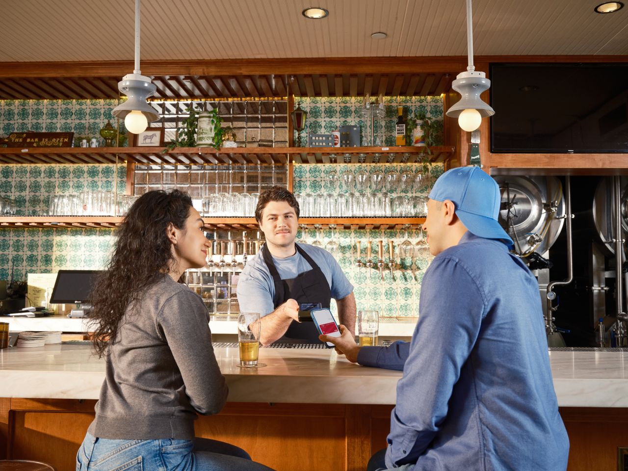 A couple uses mobile payment at a trendy bar with a bartender assisting.