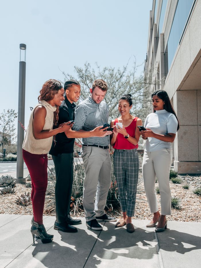 A group of diverse colleagues interacting on smartphones outside an office building.